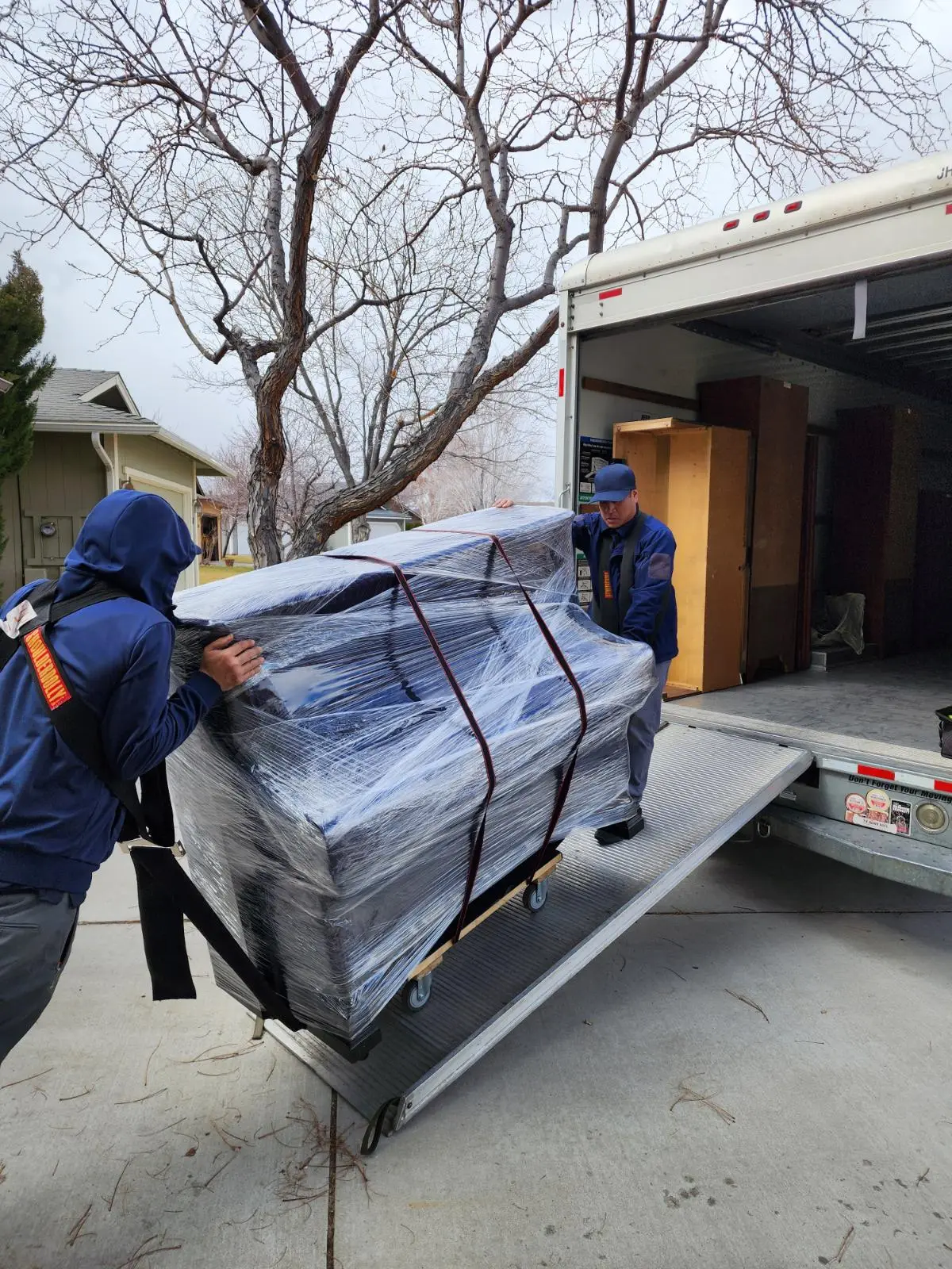 Green Echo movers loading a wrapped piano onto a moving truck ramp