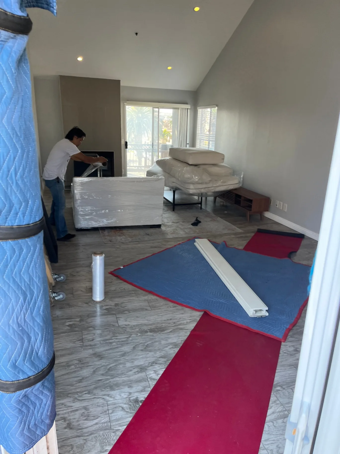 Green Echo mover shrink-wrapping a sofa in a California living room with floor runners laid down